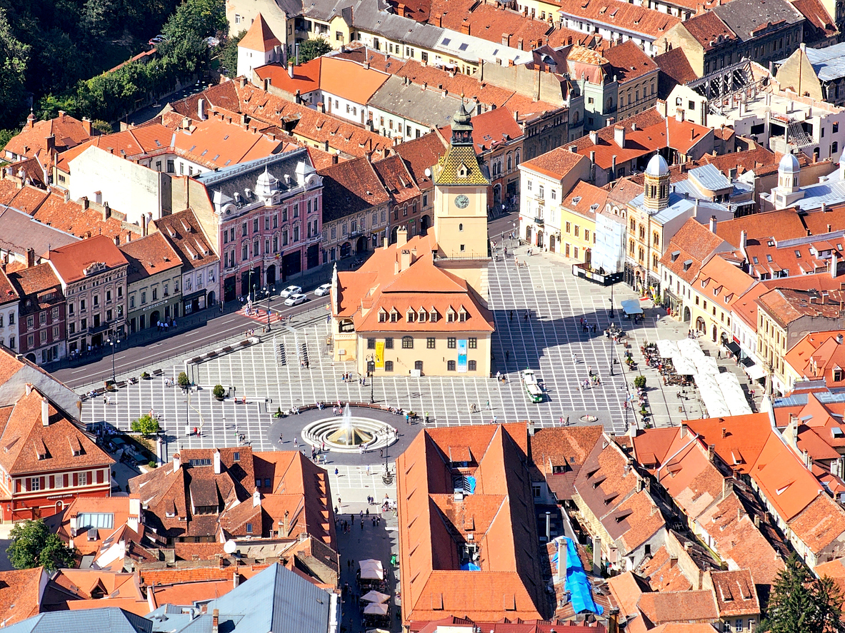 Luftaufnahme des Stadtzentrums von Brașov in Rumänien mit Marktplatz, Ratshaus und umliegenden historischen Gebäuden mit roten Dächern.
