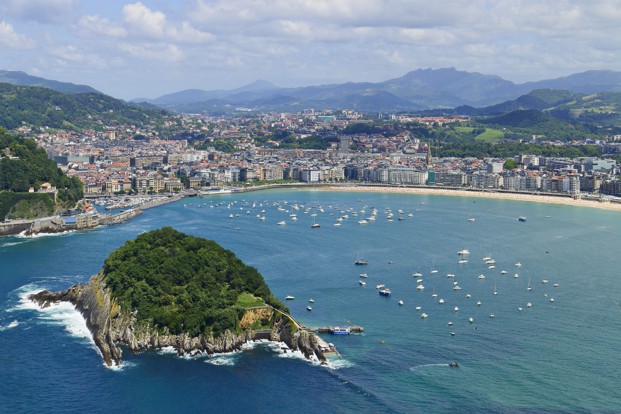Luftaufnahme der Bucht La Concha in San Sebastián mit zahlreichen Segelbooten im Wasser, umgeben von der Stadt und den grünen Hügeln im Hintergrund.