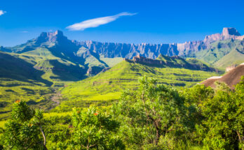 Grüne Täler und die steilen Klippen des Amphitheaters in den Drakensbergen unter blauem Himmel.