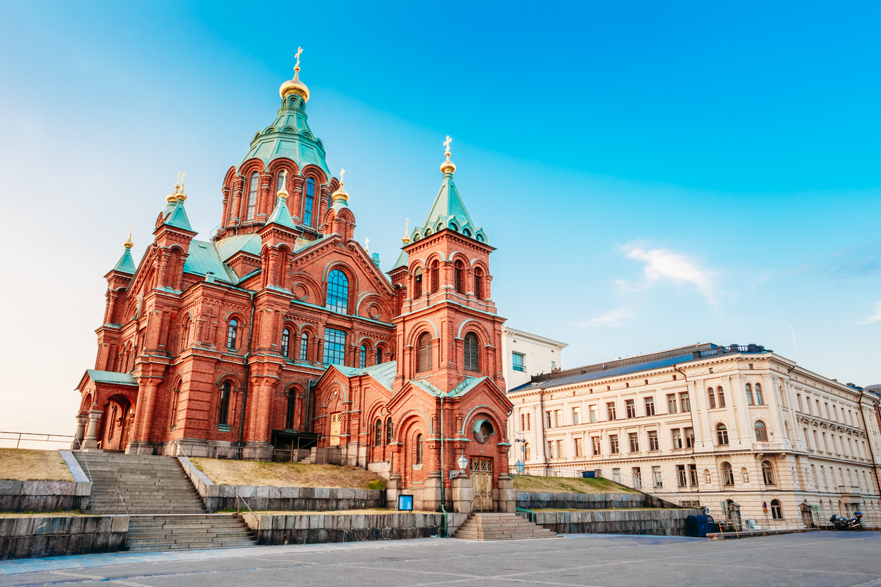 Rote Backstein-Uspenski-Kathedrale in Helsinki mit türkisfarbenen Kuppeln und blauen Himmel im Hintergrund.