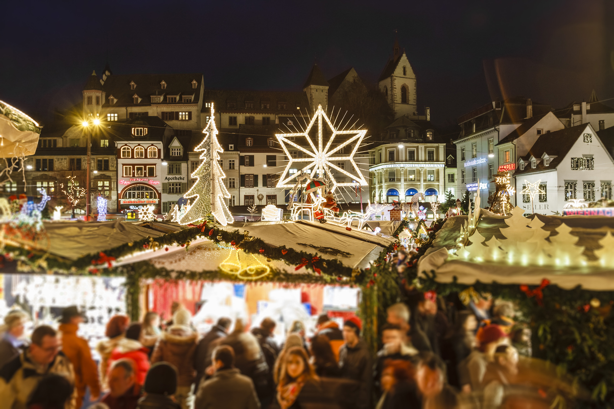 Basler Weihnachtsmarkt bei Nacht mit hell erleuchteten Ständen, großem Stern, Lichtertannenbaum und Altstadthäusern im Hintergrund