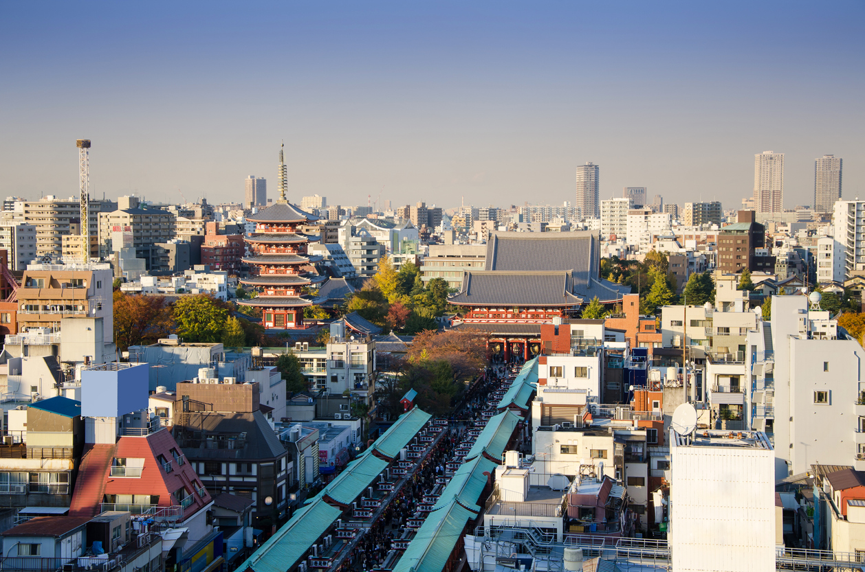 Blick auf den Sensō-ji-Tempel in Tokio mit der fünfstöckigen Pagode, dem Hauptgebäude und belebter Einkaufsstraße, umgeben von moderner Stadtarchitektur.