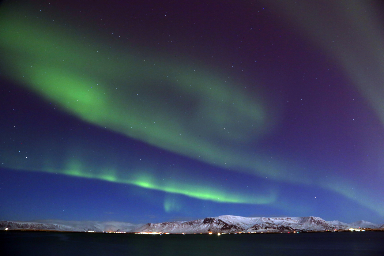 Grüne Nordlichter am Nachthimmel über Reykjavik mit verschneiten Bergen.