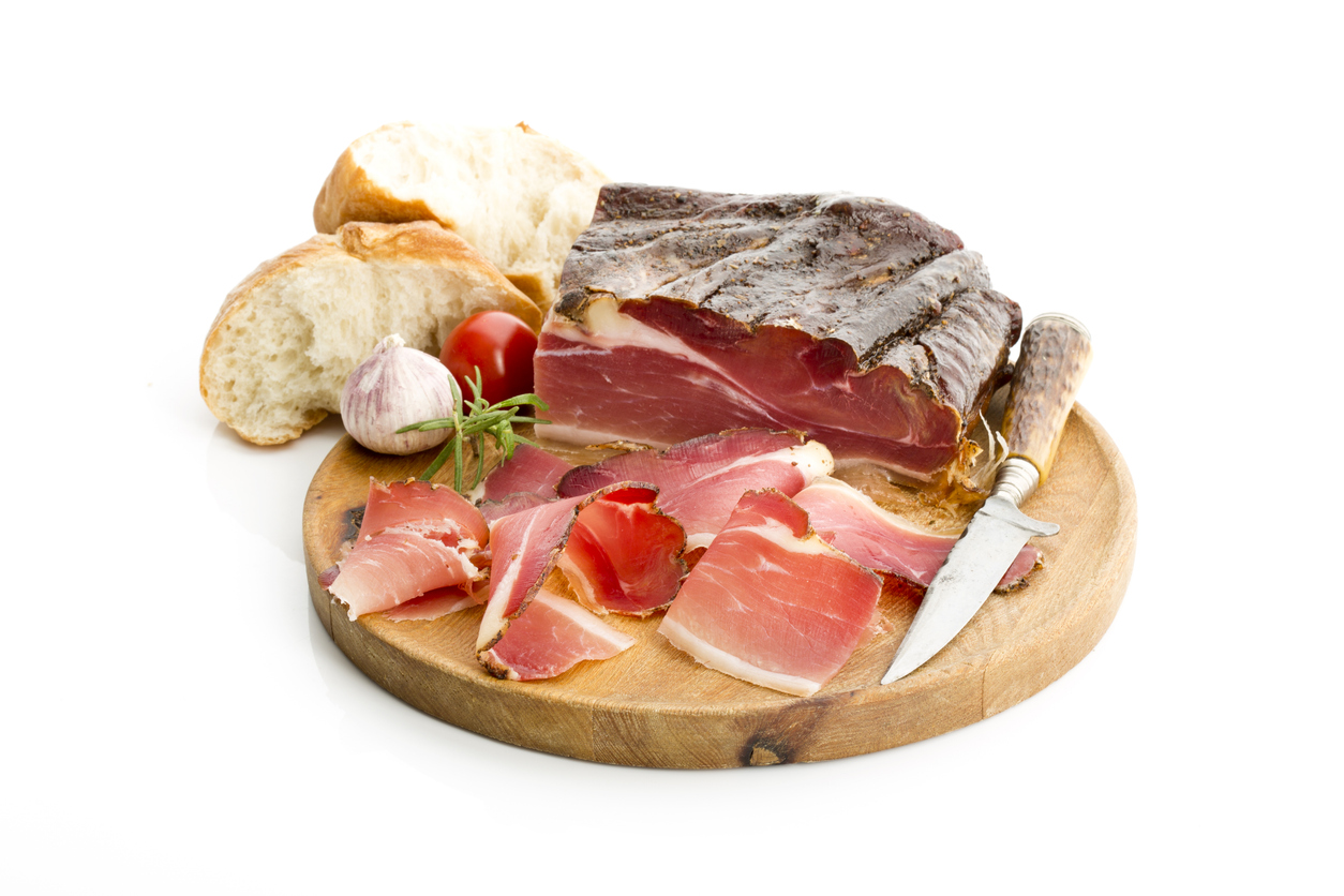 Südtiroler Schinken in Scheiben auf Holzbrett mit Brot und Messer