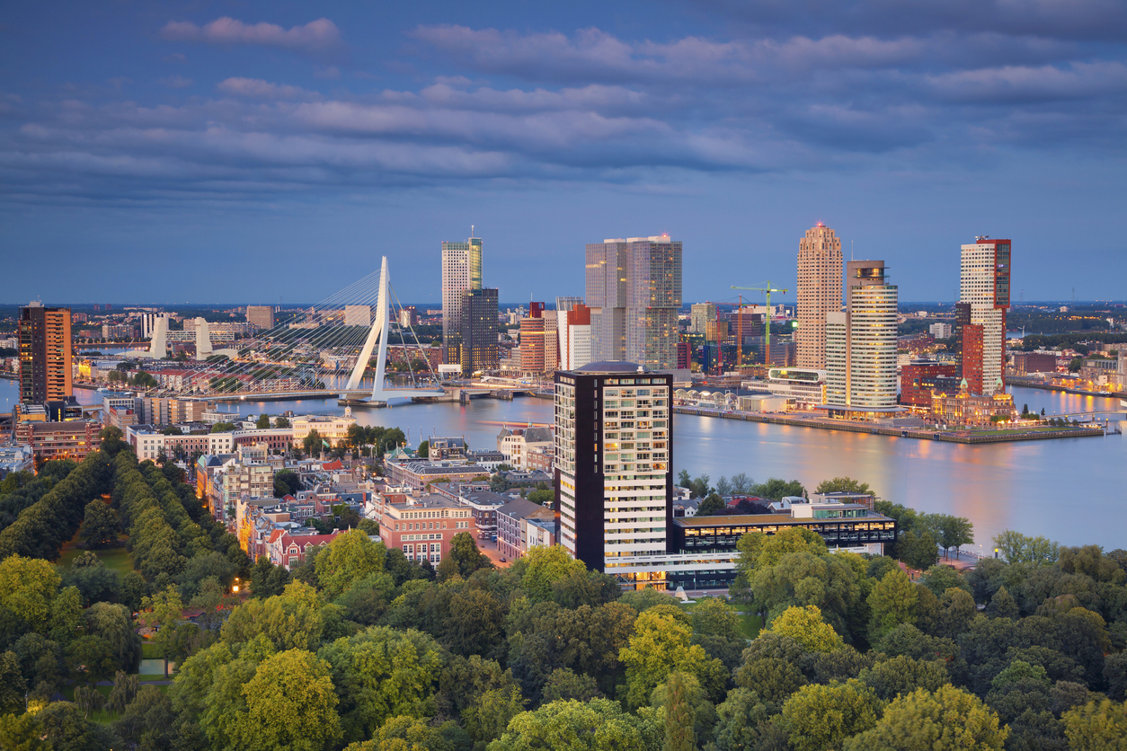 Rotterdam mit Erasmusbrücke, Hochhäusern am Kop van Zuid und Nieuwe Maas bei Abenddämmerung.