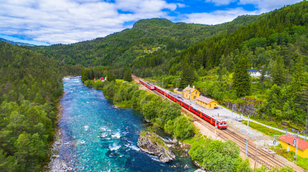 Der berühmte Panoramazug von Oslo nach Bergen fährt entlang eines Flusses durch die norwegische Landschaft.