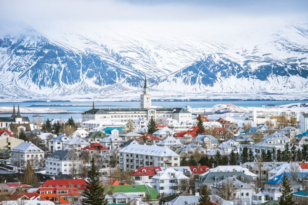 Panorama von Reykjavik im Winter mit bunten Dächern und schneebedeckten Bergen im Hintergrund.