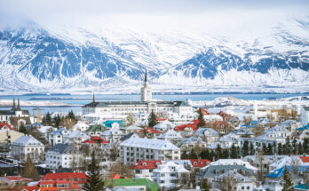 Panorama von Reykjavik im Winter mit bunten Dächern und schneebedeckten Bergen im Hintergrund.