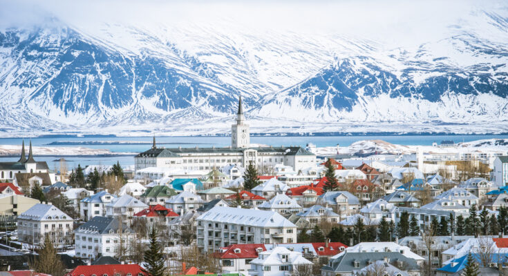 Panorama von Reykjavik im Winter mit bunten Dächern und schneebedeckten Bergen im Hintergrund.