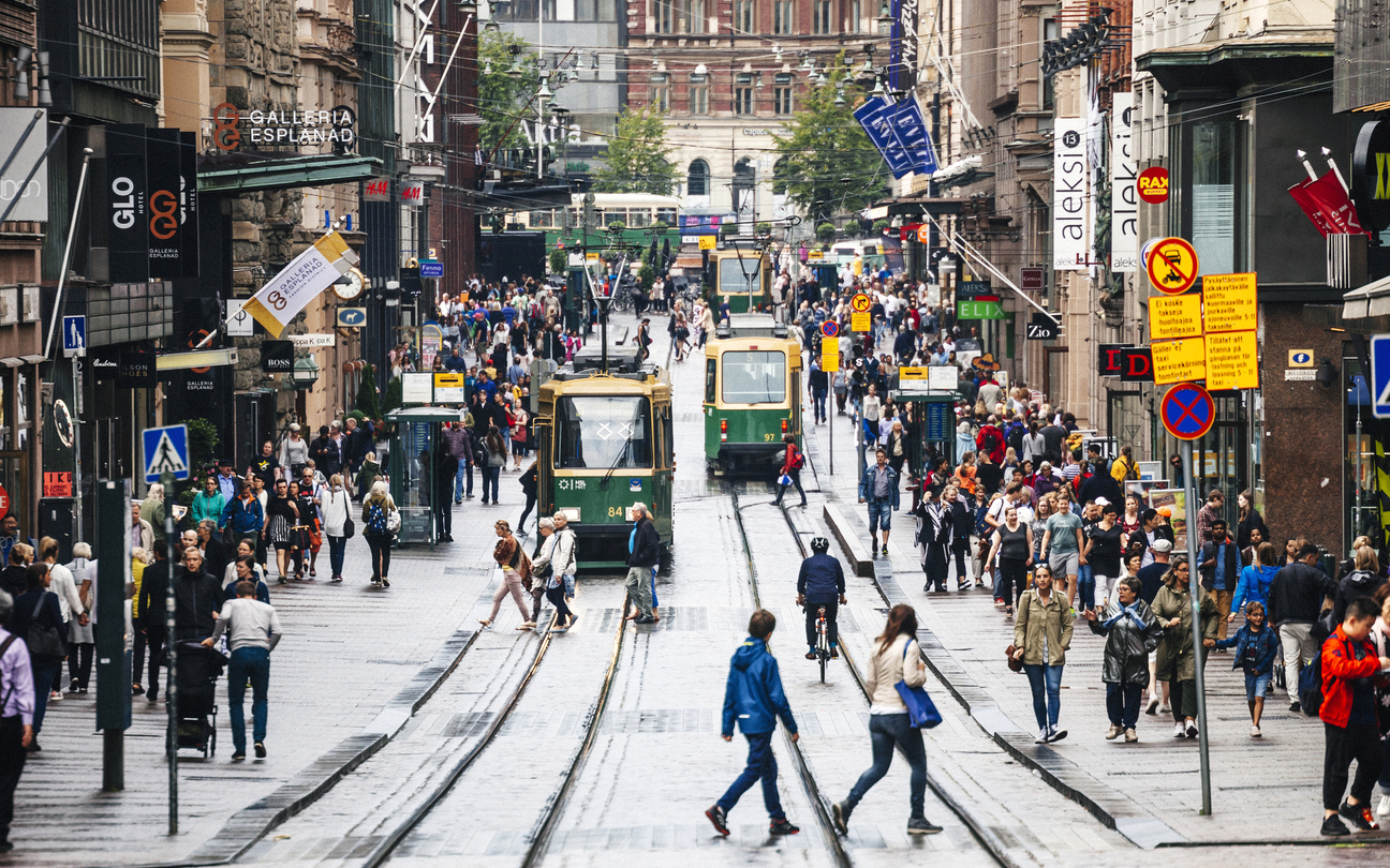 Menschen und Straßenbahnen auf einer belebten Einkaufsstraße im Zentrum von Helsinki.