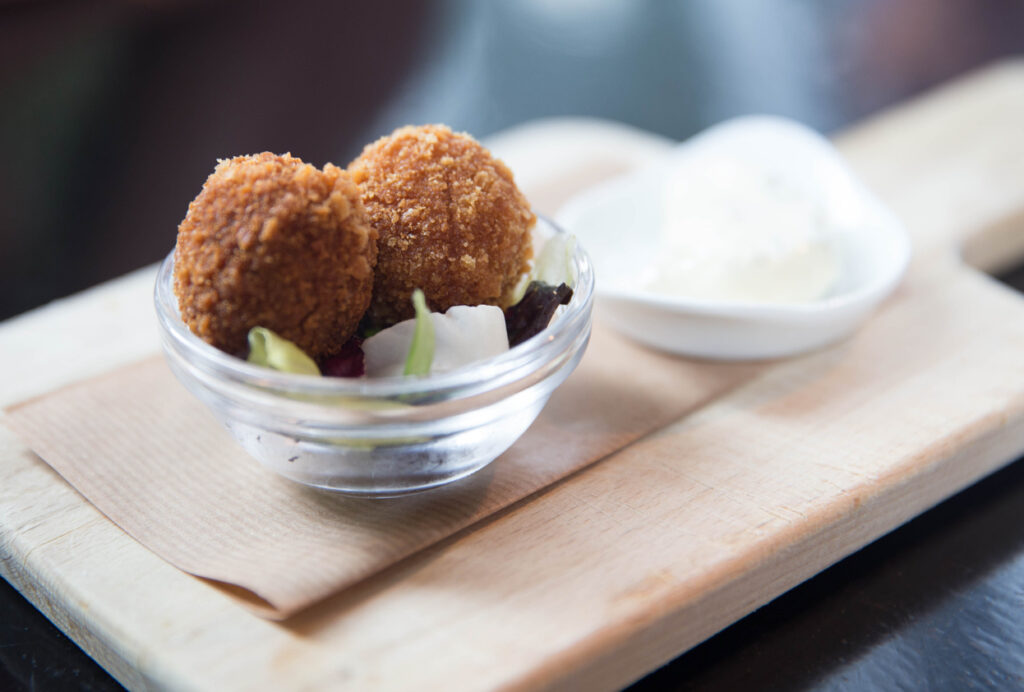 Niederländische Bitterballen, zwei knusprig frittierte Fleischbällchen in einer kleinen Schale mit Dip und Beilage serviert.