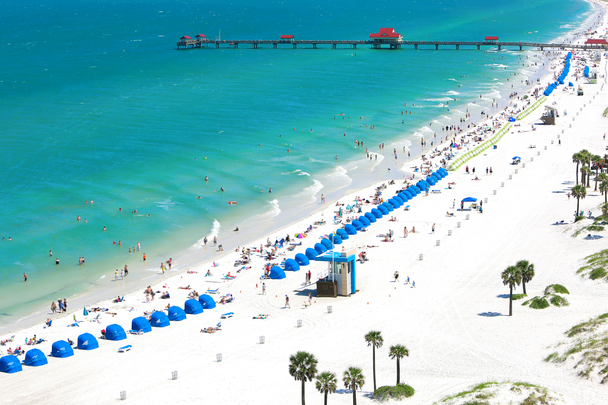Luftbild von Clearwater Beach: weißer Sand, türkisfarbenes Wasser, Reihen blauer Cabanas und Pier 60.