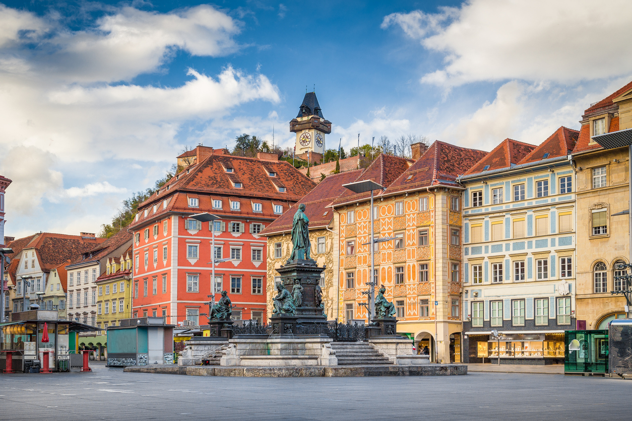 Historischer Hauptplatz mit bunten Fassaden, Brunnen und Uhrturm am Schlossberg.