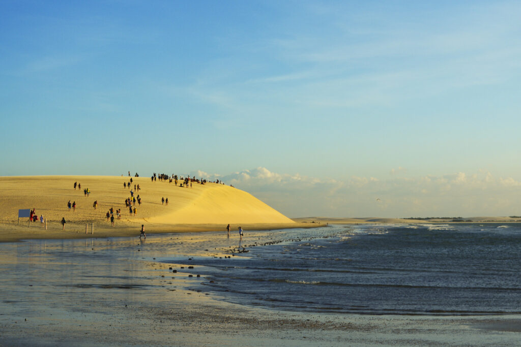 Große Sanddüne mit vielen Besuchern am Meer bei tiefstehender Sonne in Jericoacoara, Brasilien.