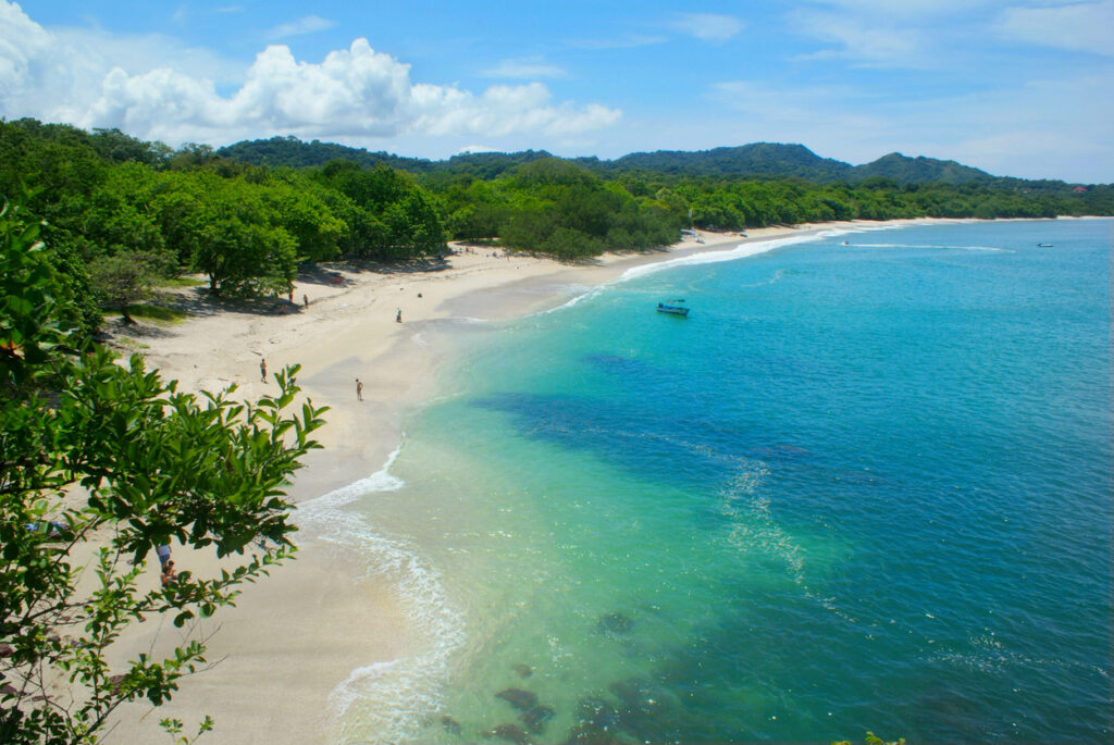 Bogenförmiger Strand mit weißem Muschelsand, klarem türkisblauem Wasser und grünem Küstenwald in Costa Rica.