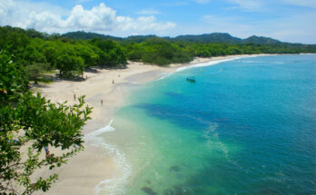 Bogenförmiger Strand mit weißem Muschelsand, klarem türkisblauem Wasser und grünem Küstenwald in Costa Rica.