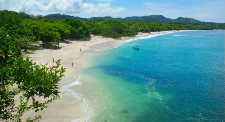 Bogenförmiger Strand mit weißem Muschelsand, klarem türkisblauem Wasser und grünem Küstenwald in Costa Rica.