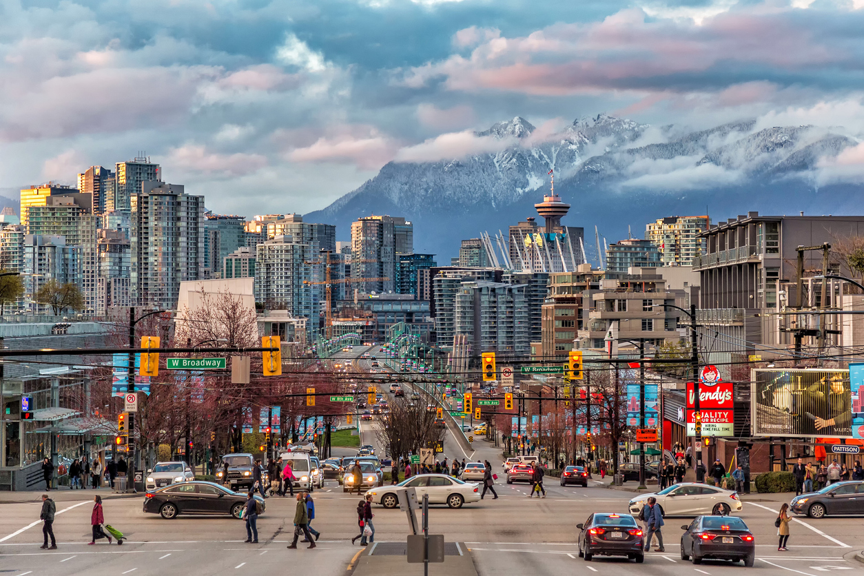 Straßenszene auf West Broadway mit Verkehr, Fußgängern und den schneebedeckten North Shore Mountains.