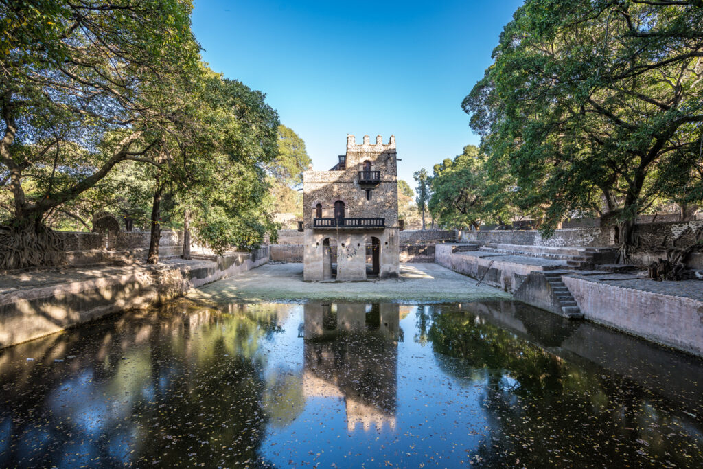 Steinpavillon mit Arkaden am Becken, umgeben von alten Bäumen.