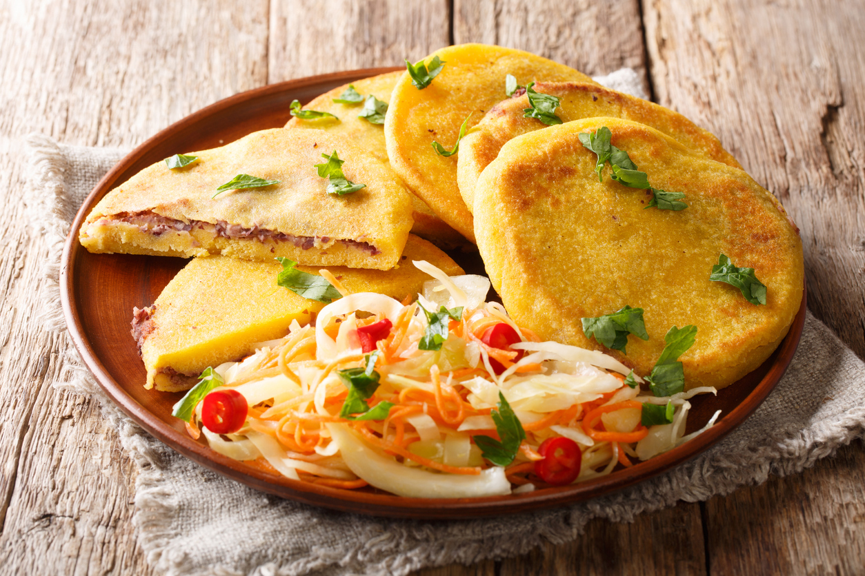 Goldbraun gebratene Pupusas mit Bohnenfüllung, daneben pikantes Curtido aus Weißkohl, Karotten, Zwiebeln und Chili auf rustikalem Teller.