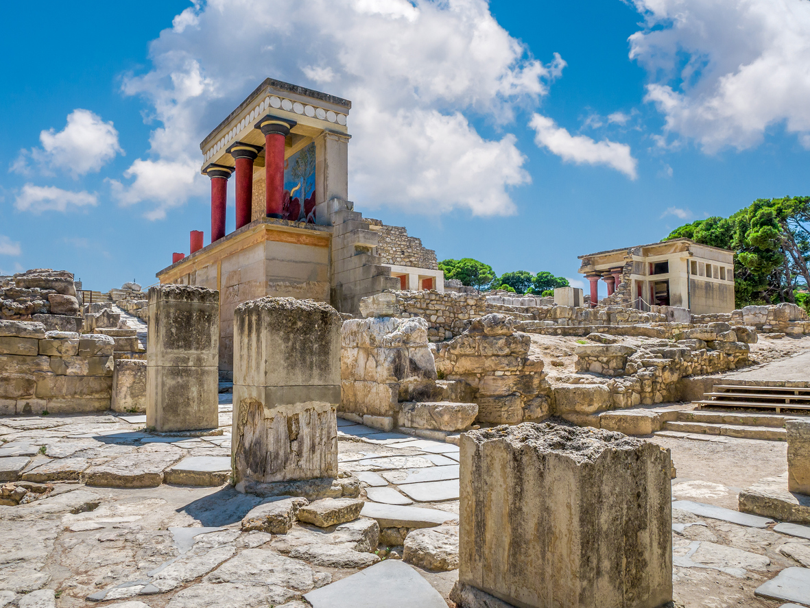 Rekonstruierte rote Säulen und Ruinen des Palasts von Knossos unter blauem Himmel.