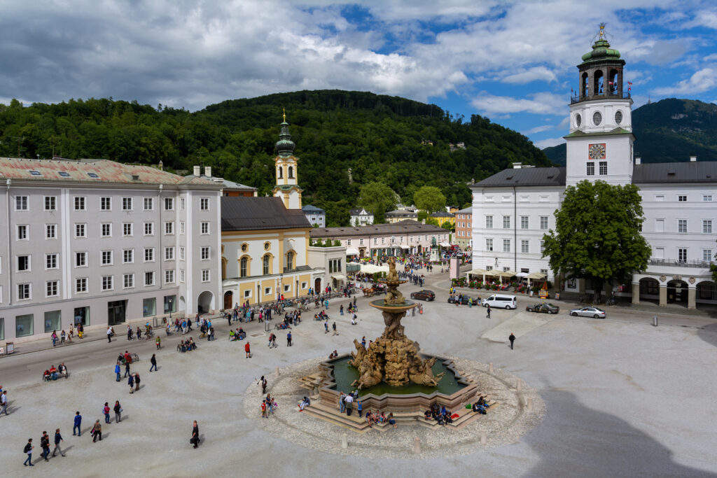 Barocker Residenzbrunnen auf dem Residenzplatz mit Turm und Bergkulisse.