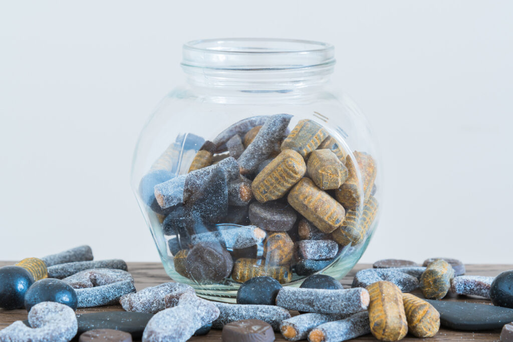 Glas mit gemischten salzigen Lakritzbonbons (Salmiakki) auf Holztisch, einige Stücke davor.