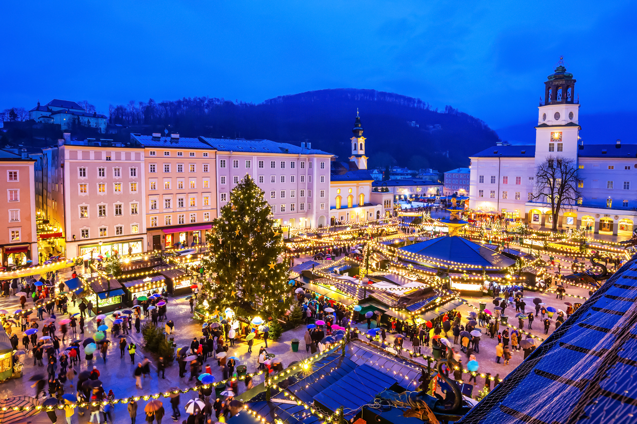 Beleuchteter Weihnachtsmarkt mit großem Baum, Ständen und vielen Besuchern in Salzburg.