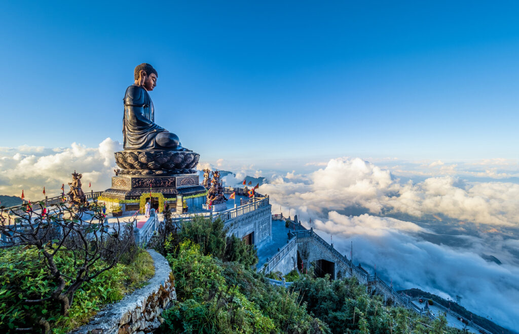 Sitzende Bronze-Buddha-Statue am Fansipan-Gipfel mit Tempelterrassen und Wolkenmeer bei Sa Pa.