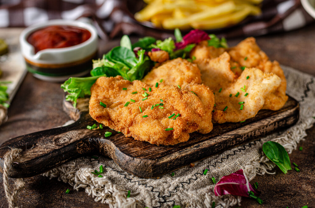 Paniertes, goldbraun gebratenes Schnitzel auf Holzbrett mit Salatgarnitur.