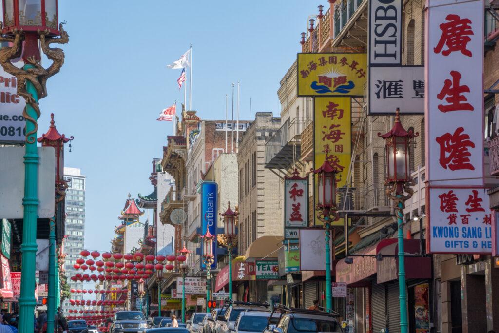 Belebte Straße in San Franciscos Chinatown mit roten Laternen, traditionellen Lampen, Pagodendächern und vielen Geschäftsschildern.