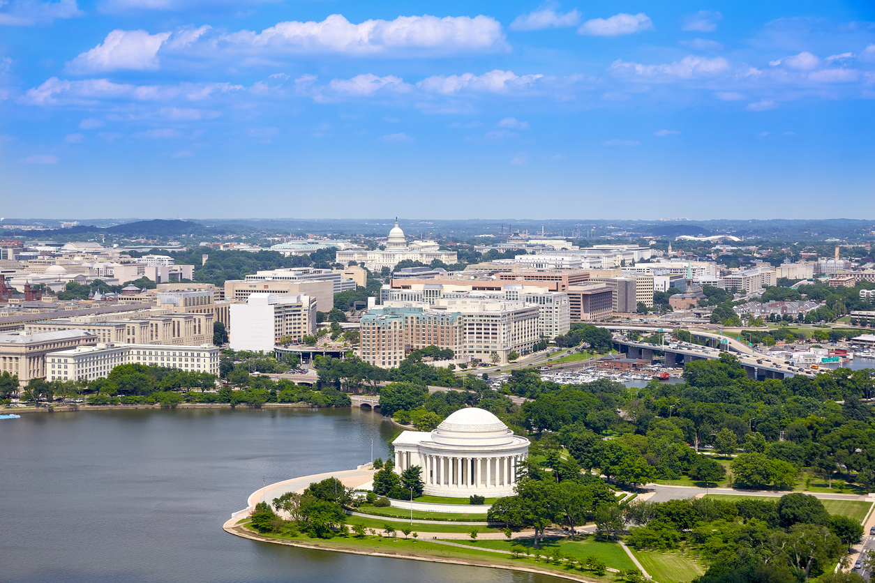 Luftaufnahme von Washington, D.C. mit dem Jefferson Memorial am Tidal Basin im Vordergrund und dem Kapitol in der Ferne unter blauem Himmel.