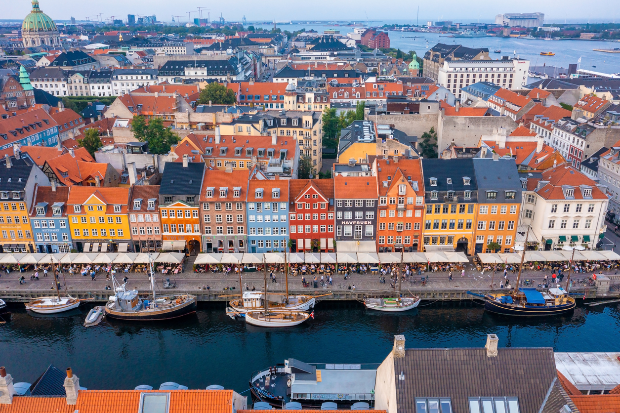 Luftaufnahme des Nyhavn-Piers mit farbigen Fassaden, vollen Straßencafés und festgemachten Booten am Kanal in Kopenhagen.