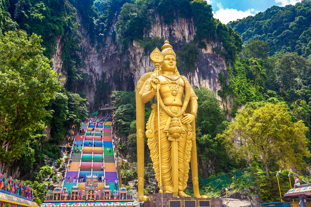 Goldene Murugan-Statue vor bunten Treppen und Felswand