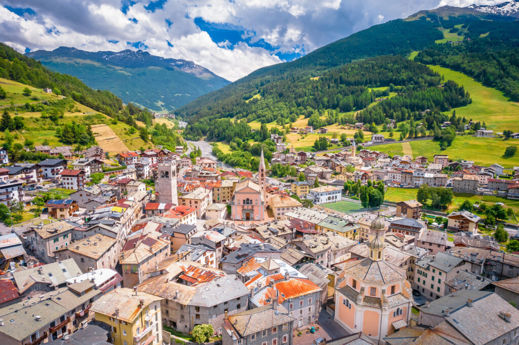 Luftaufnahme von Bormio mit Kirchtürmen, Altstadtdächern und grünen Berghängen.