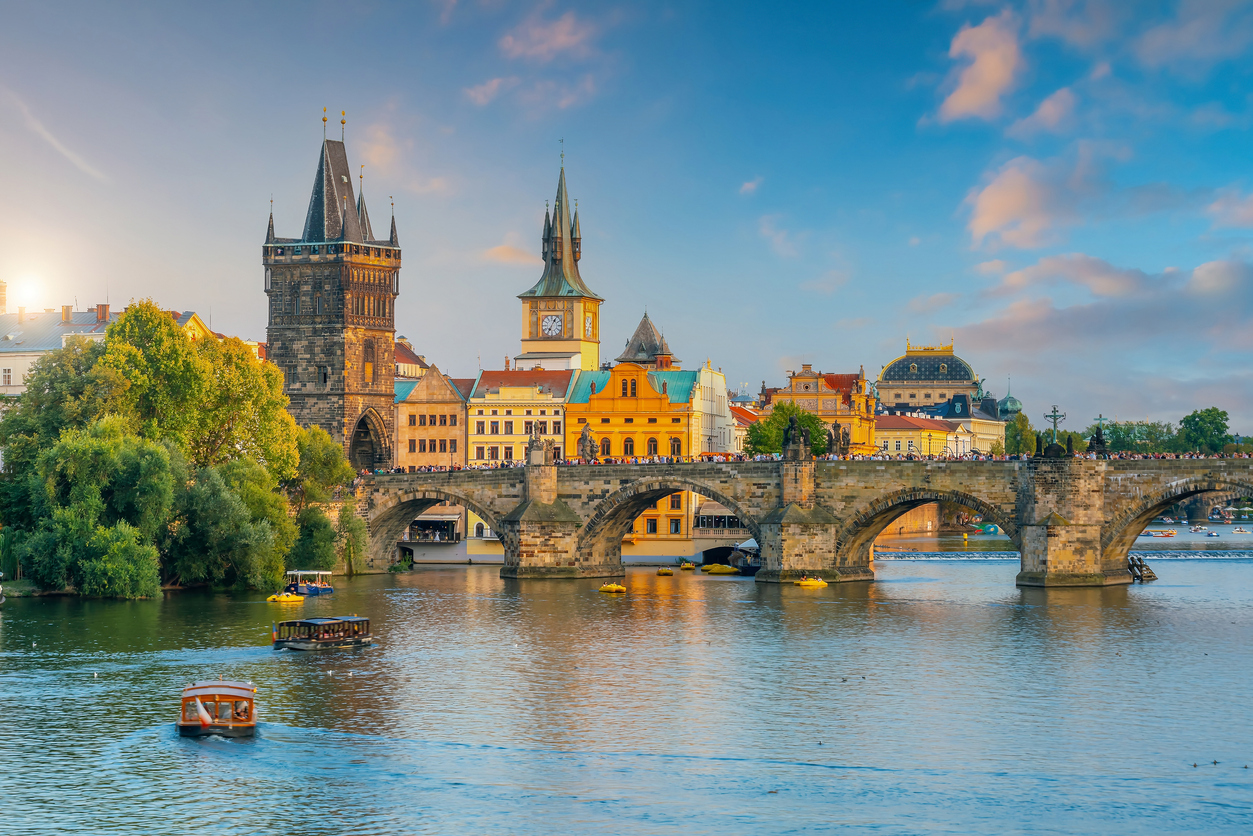Blick auf die Karlsbrücke über die Moldau mit Altstadttürmen, Booten und warmem Abendlicht.