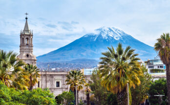 Zwischen hohen Palmen ragt ein Kathedralturm auf, dahinter steht der schneebedeckte Vulkan Misti.