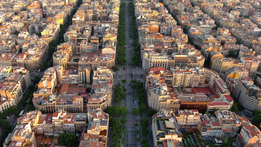 Von oben sieht man die baumbestandene Mittelachse des Passeig de Gràcia, flankiert von Eixample-Blocks mit Innenhöfen und Kreuzungen im Schachbrettmuster.