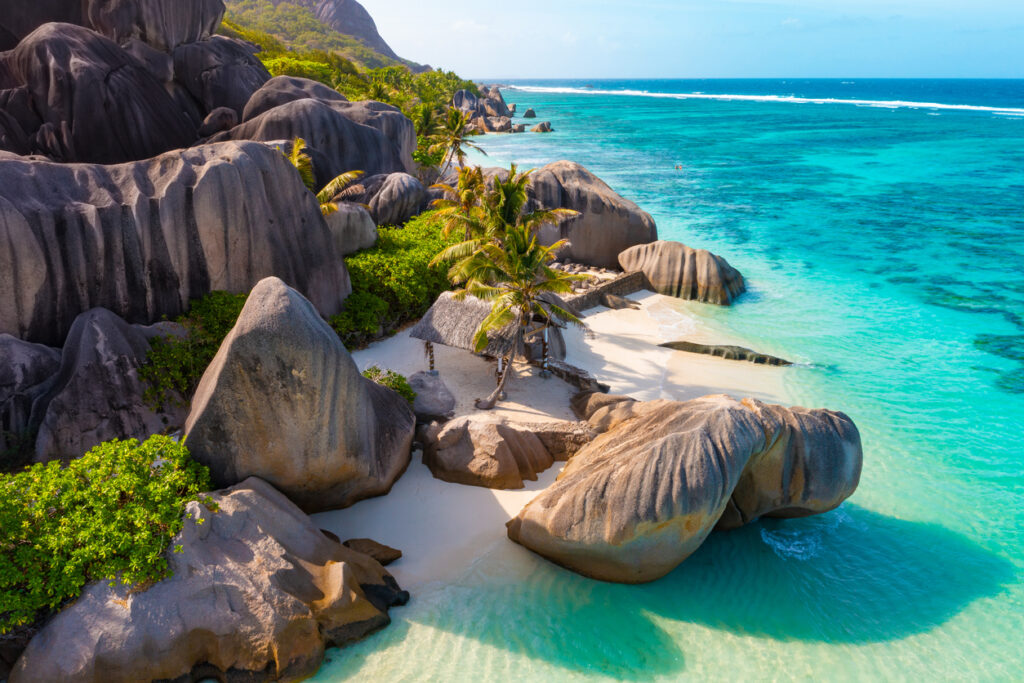 Rundgeschliffene Granitblöcke rahmen weißen Sand und klares, türkisblaues Meer.