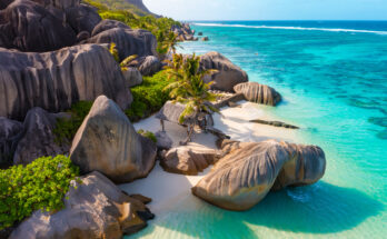 Rundgeschliffene Granitblöcke rahmen weißen Sand und klares, türkisblaues Meer.