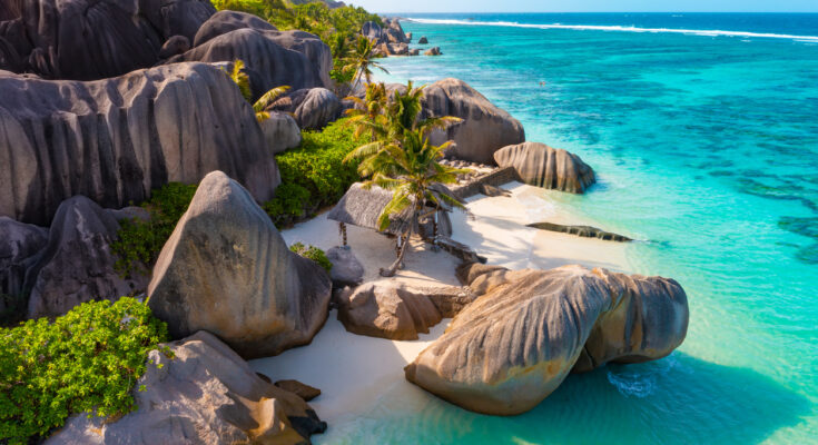 Rundgeschliffene Granitblöcke rahmen weißen Sand und klares, türkisblaues Meer.