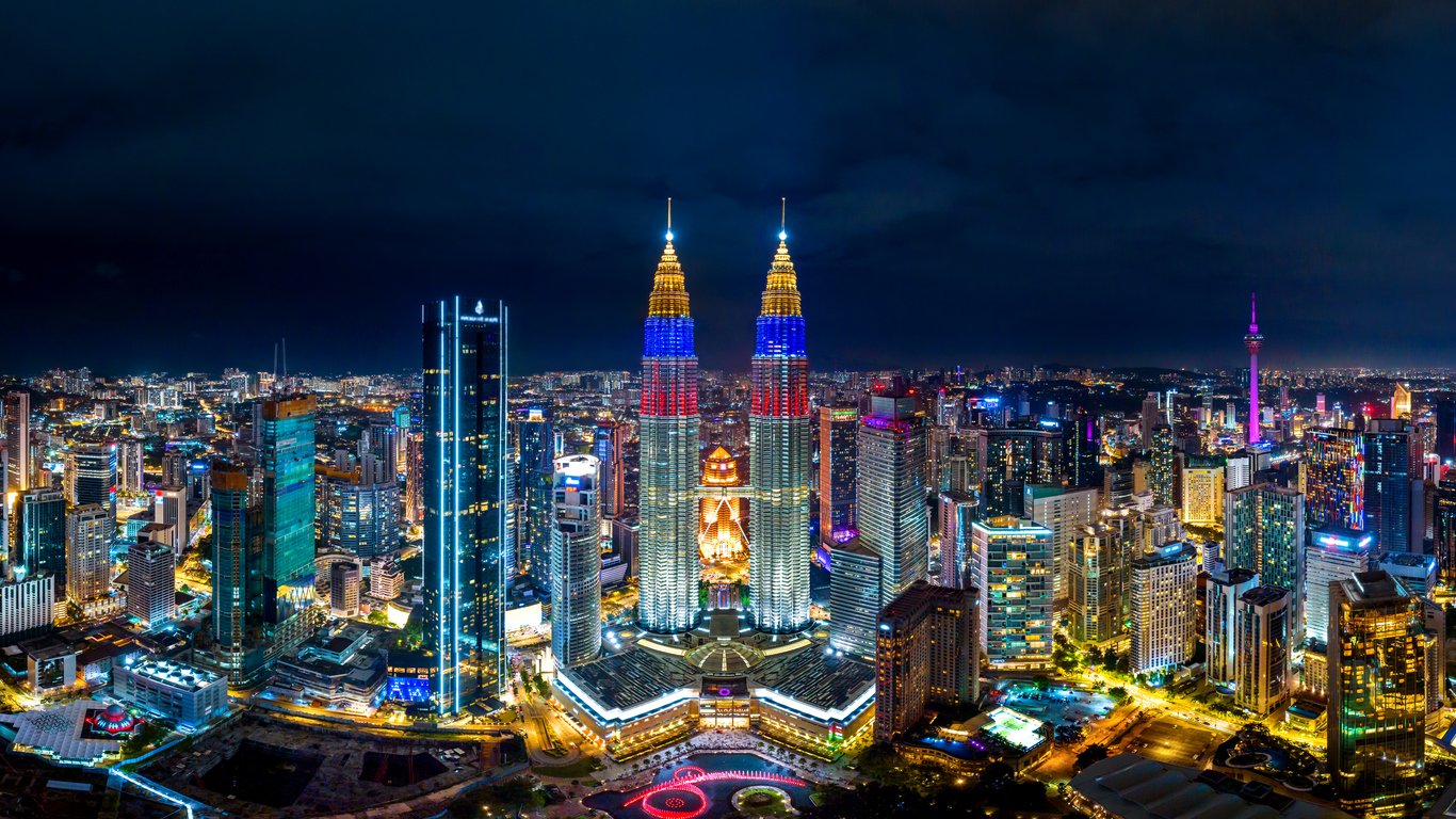 Nachtpanorama mit beleuchteten Petronas Towers und dem KL Tower über der Stadt.