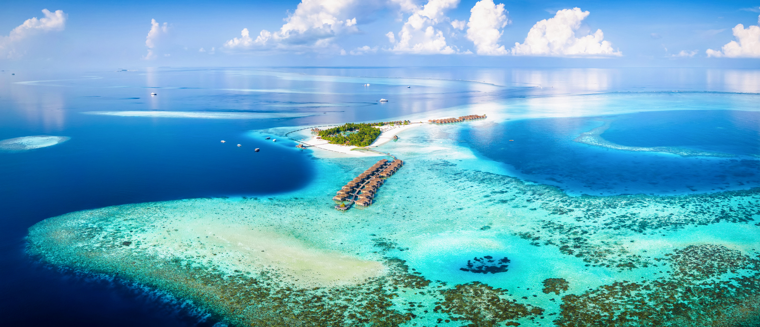 Luftaufnahme einer kleinen Insel mit Stegen und Wasserbungalows in türkisfarbener Lagune.