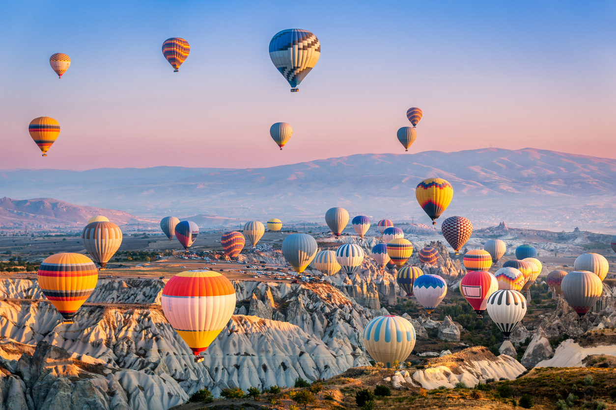 Viele bunte Ballons schweben bei Sonnenaufgang über Tuffstein-Tälern.