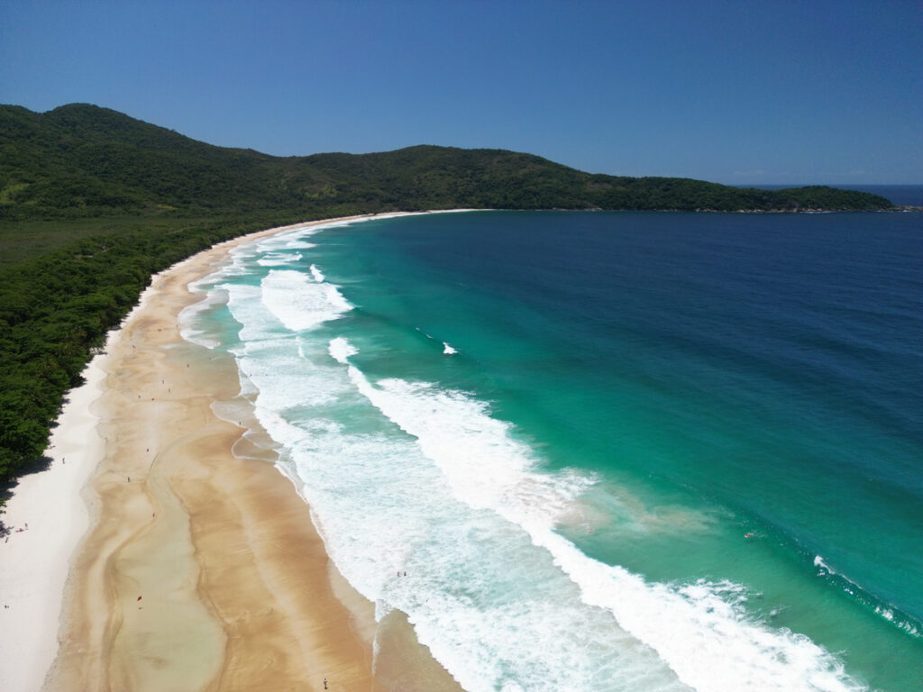 Langer weißer Sandstrand mit türkisblauem Wasser und sanfter Brandung am Praia de Lopes Mendes auf Ilha Grande, Brasilien.