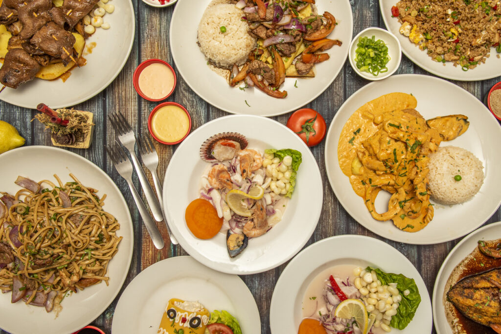 Draufsicht auf Teller mit peruanischen Klassikern wie Ceviche, Lomo Saltado, Ají de Gallina, Arroz Chaufa und Anticuchos.