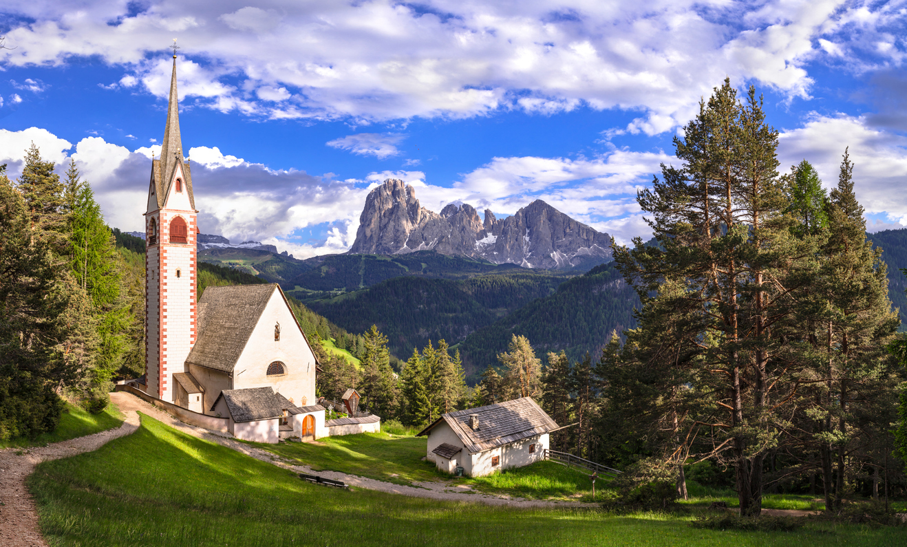 Bergkirche mit spitzem Turm über Ortisei vor der Langkofelgruppe in den Dolomiten.