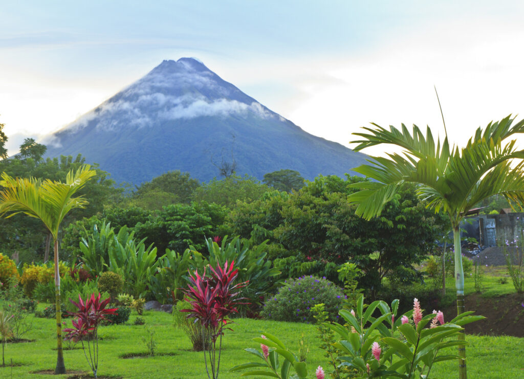 Kegelförmiger Arenal mit Wolkenkranz über tropischem Garten in La Fortuna.