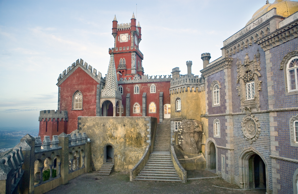 Innenhof des Palácio da Pena mit rotem Uhrturm, gelbem Trakt, blauer Azulejo-Fassade und breiter Freitreppe.