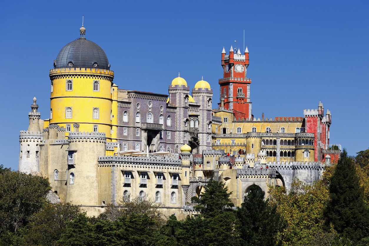 Gelber Rundturm und roter Uhrturm des Palácio da Pena in Sintra vor klarem blauem Himmel.